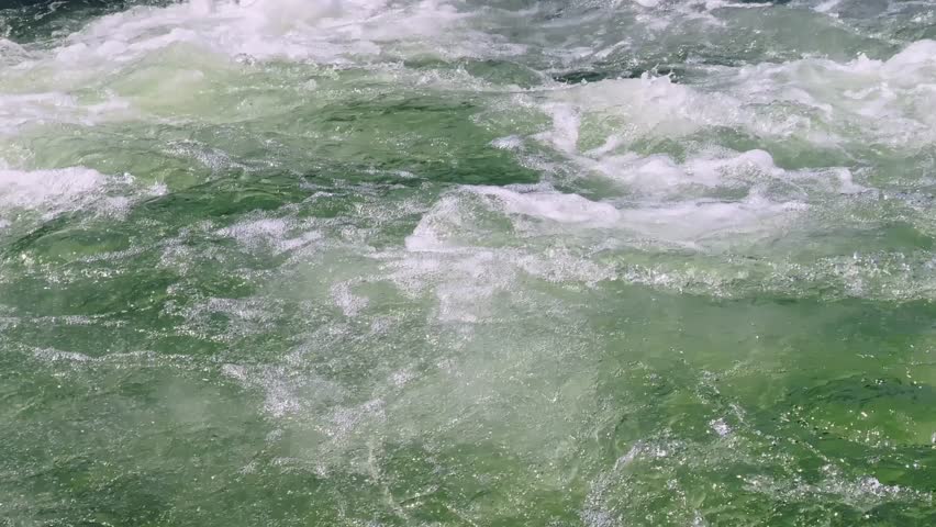 Close-up of fast turquoise river rapids with white foam, swirling water and strong current in a natural outdoor stream.