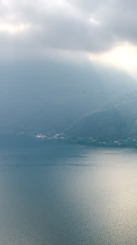 Clouds move over a calm lake as sun rays break through, illuminating water and hills