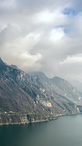 Clouds move over rugged mountain slopes above a calm lake in a scenic landscape