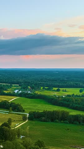 Clouds move over a rural landscape with fields, forests, and distant farm buildings