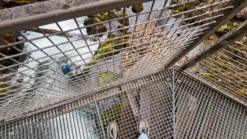 POV from a metal walkway above Golling Waterfall, showing rushing whitewater, safety railings, mossy rocks, forest slopes, and valley views.