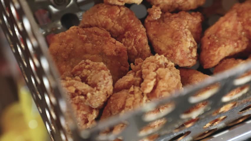 Close-up of crispy fried chicken pieces inside a metal frying basket in a kitchen setting