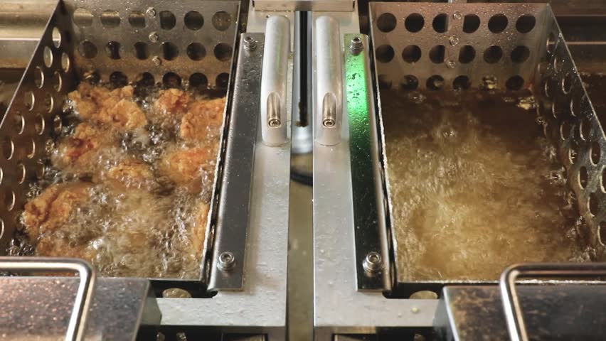 Overhead view of two deep fryers with bubbling hot oil and frying chicken in metal baskets in a commercial kitchen setting