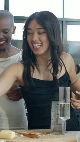 Vertical video: Hearing friend, woman in black dress reaching to set red drink on island with pizza. Kitchen, friends, elegant, lifestyle, culinary, celebration, vertical video