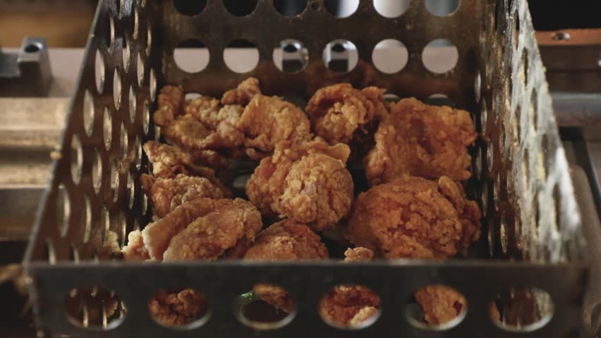 Close-up of crispy fried chicken pieces inside a metal frying basket in a commercial kitchen