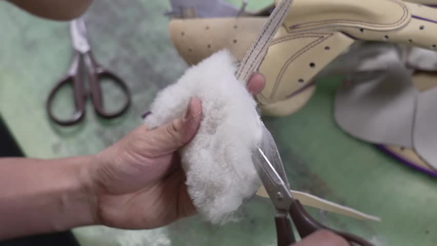 Craftsman stuffing soft cotton wadding into a baseball glove finger with scissors nearby