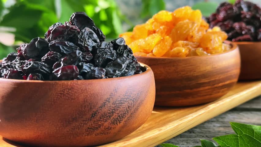 Three raisin varieties in wooden bowls with slow rightward camera movement and shifting focus on a rustic tabletop