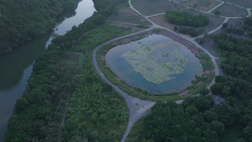 Aerial view of a tranquil lake surrounded by lush greenery in a Vietnamese countryside. The lake is surrounded by a dirt path and a forest, creating a serene and peaceful atmosphere.