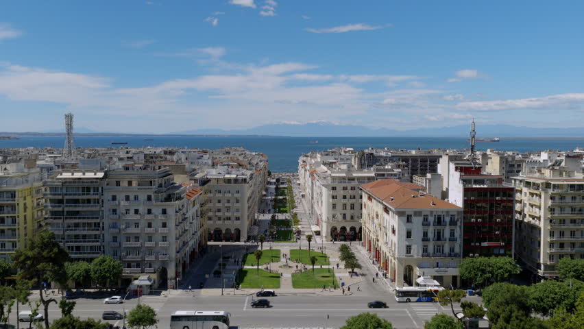 Aerial view down Aristotelous Square toward the sea, showing neoclassical buildings, green gardens, and Thessaloniki