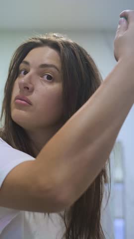 Brunette woman with long hair applies a thermal protection spray before blow-drying, practicing gentle hair care at home to protect against heat, breakage, and loss of color.