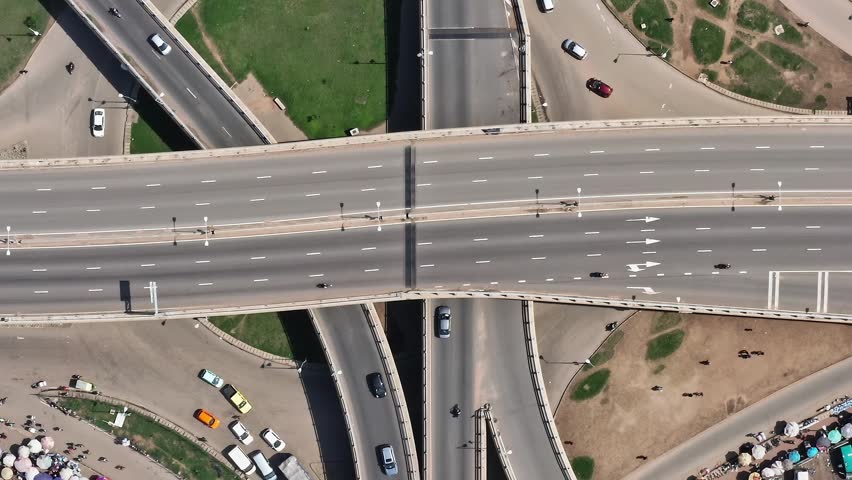 Vehicles move along a multi-level road structure in Accra, Ghana. People are present near the edges, and the cityscape shows signs of daily urban activity and movement.