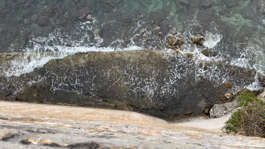Waves crashing against rocky shoreline viewed from above