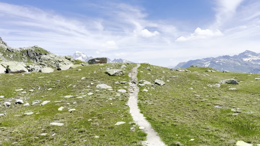 Alpine hiking trail winding over a grassy high-altitude ridge toward distant snow-capped peaks above Obergesteln in the Goms valley, Valais, Swiss Alps