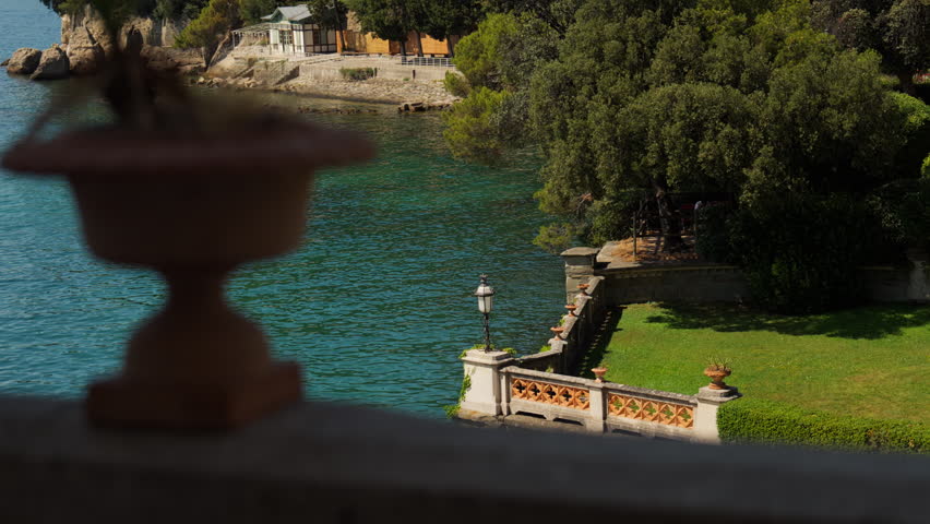 View from the gardens of Miramare Castle in Trieste, with turquoise Adriatic water, stone balustrades, green lawns, and a wooded shoreline.