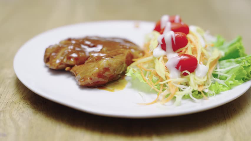Juicy grilled meat steak glazed with savory brown gravy served on a white plate with fresh shredded vegetable salad and cherry tomatoes. Healthy protein dinner meal with creamy white dressing.