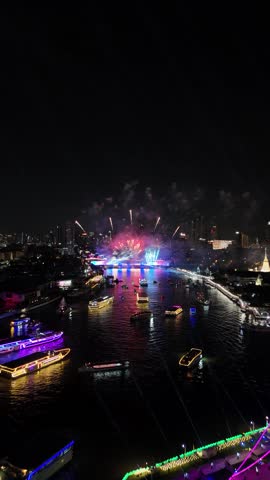 Luminous fireworks exploding in vibrant colors over a bustling city river in Bangkok, Thailand at night. With illuminated boats watching the show and reflections creating a mesmerizing scene of celebration and festivity.