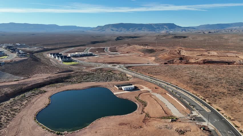 An Aerial view of new housing lots and roads around a large, dark retention pond in a dry, mountainous desert landscape.