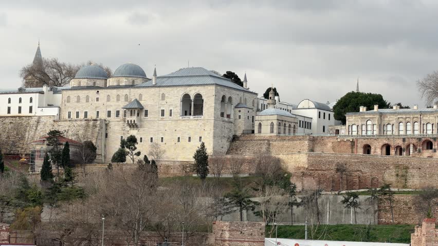 Establishing panoramic shot of the monumental Topkapi Palace, showcasing intricate Ottoman architecture, domes, and stone walls overlooking the landscape in Istanbul, Turkey.
