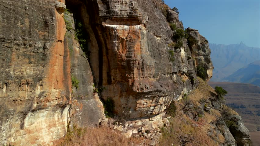 Cinematic drone footage flying past a rocky foreground to reveal the dramatic peaks of the Drakensberg Mountains in South Africa. Scenic aerial landscape showcasing the rugged beauty of one of Africa