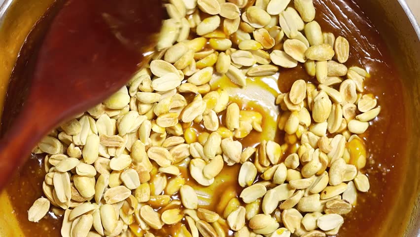 woman making caramel with roasted peanuts on pan 