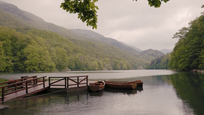 Serene mountain Biogradsko lake with a wooden pier and moored boats reflecting on the calm water. Lush green forest covering the surrounding hills