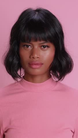 Southeast Asian woman lowers head with upset expression, looks directly forward with disappointed face, crosses arms over chest while posing against monochrome pink background in professional studio.
