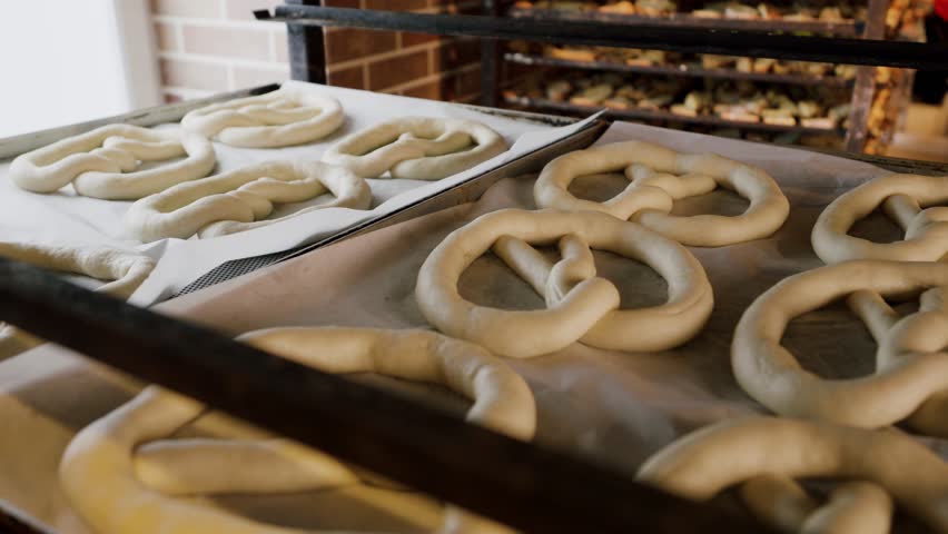 Shaped pretzels sit on parchment paper in a bakery, highlighting the dough