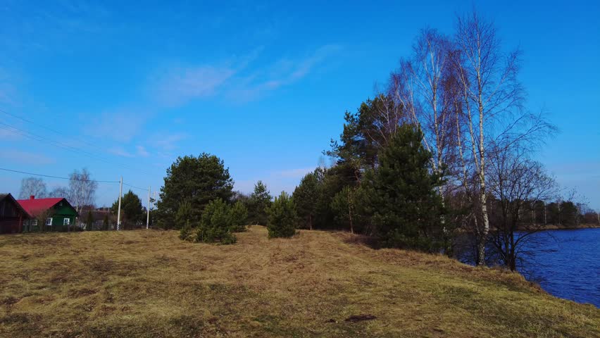 Trees and grass are visible in a rural area close to a lake. The sky is blue and clear with few clouds. The setting appears calm and natural during daytime.