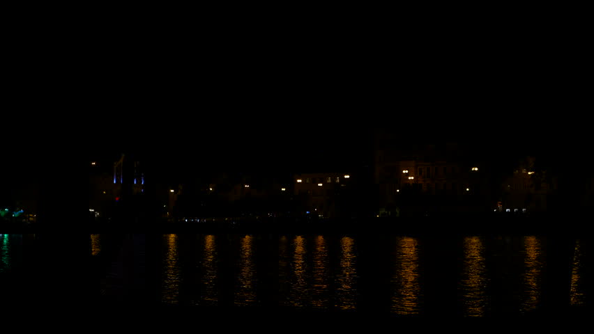 Silhouette walking across river at night. Lights reflect on the water at night, creating a serene and tranquil atmosphere in the urban landscape