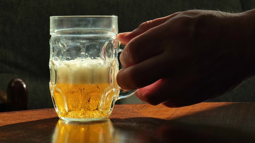 Man Holding Glass Mug of Cold Beer While Relaxing at Home.A traditional glass beer mug in hand. 4k footage