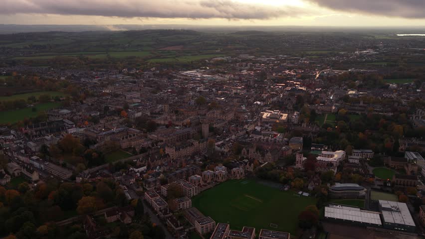 An aerial view of the city of Oxford at sunset in the United Kingdom, showcasing historic university buildings, glowing rooftops, and wide landscapes