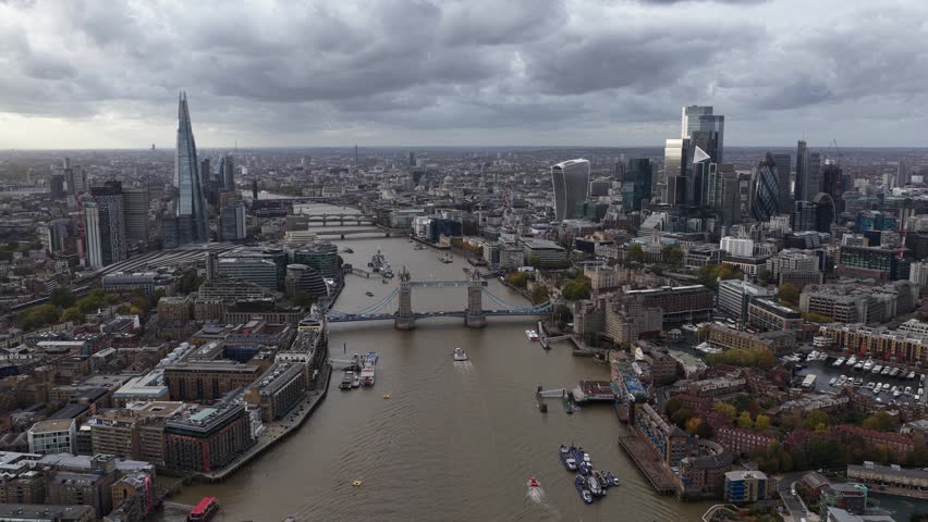 An aerial drone view of Tower Bridge stretching across the River Thames in London, showing the skyline, boats, and surrounding historic