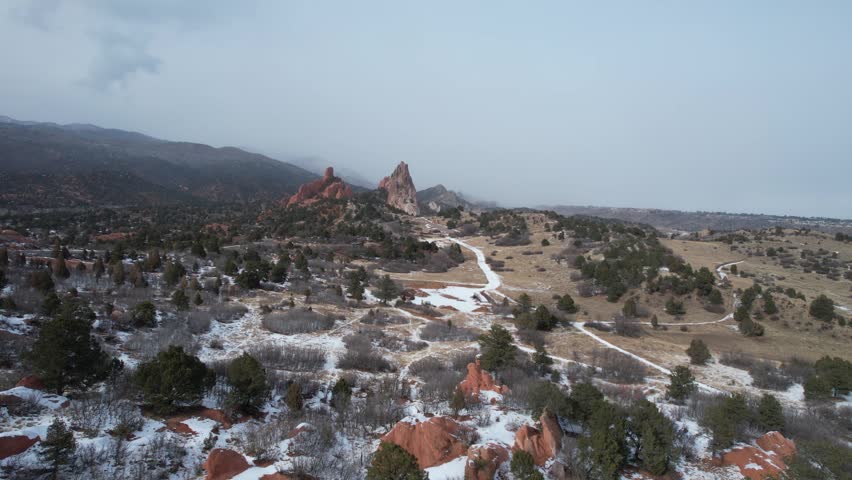 A drone view of snow-covered trails and rolling terrain leading toward the red rock formations of Garden of the Gods in winter in Colorado, USA