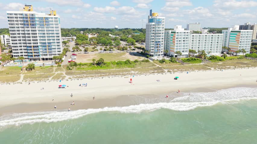 Beachfront view of Myrtle Beach, South Carolina, showcasing sandy shore, ocean waves, and high-rise hotels under a clear blue sky