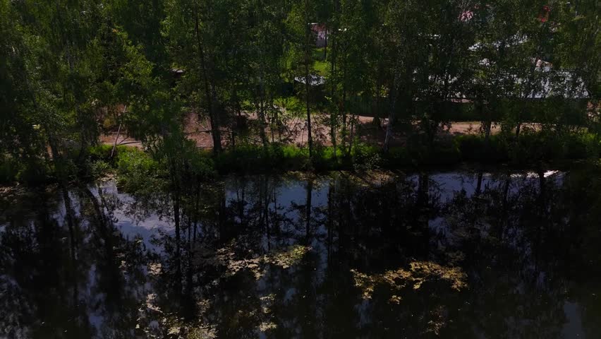 A return flight, gaining altitude above a beautiful lake surrounded by forest and country houses on a sunny summer day. Lake Kedr, Novosibirsk, Russia.