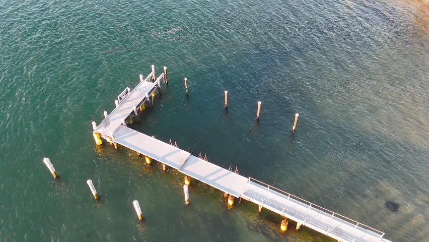 High angle drone shot of a wooden pier over clear turquoise water in Nelson Bay.