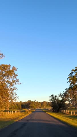 A low-angle tracking shot moves along a quiet country road during a clear sunset.
