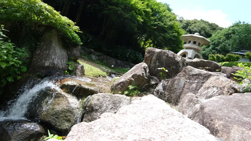 Small Garden Waterfall Flowing Between Large Rocks in a Lush Green Landscape