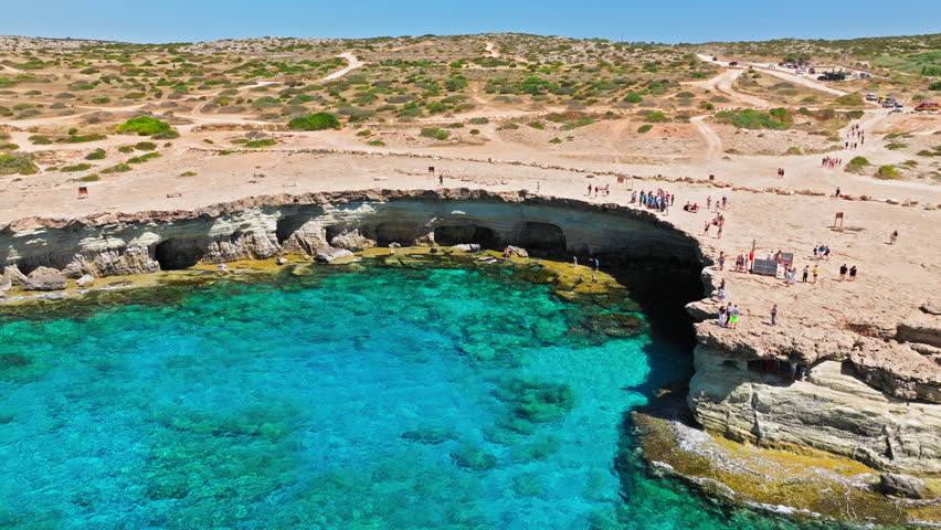 Aerial view of Cape Cavo Greco cliffs and sea caves in Cyprus. Clear blue water, natural cave openings and rocky coastline form a striking coastal view.