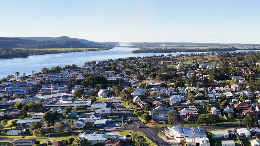 Wide aerial shot of a sunny suburban landscape beside a large river under blue skies.