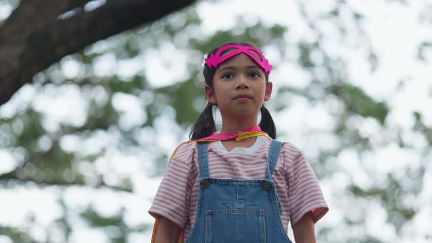 Cute Asian children playing superhero roleplay with colorful cape and mask running in outdoor green park. Kids imagination, creative future dream, and brave hero inspiration.
