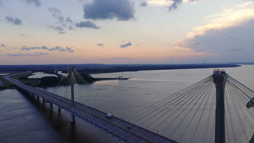 Clark Bridge spans the Mississippi River between Alton, Illinois and West Alton, Missouri beneath a blue hour sky, showcasing its cable stayed design over calm water, static aerial shot.