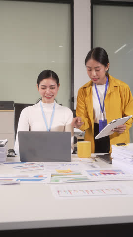 Two women working together in an office with laptop, documents and tablet, smiling during a team meeting at a desk