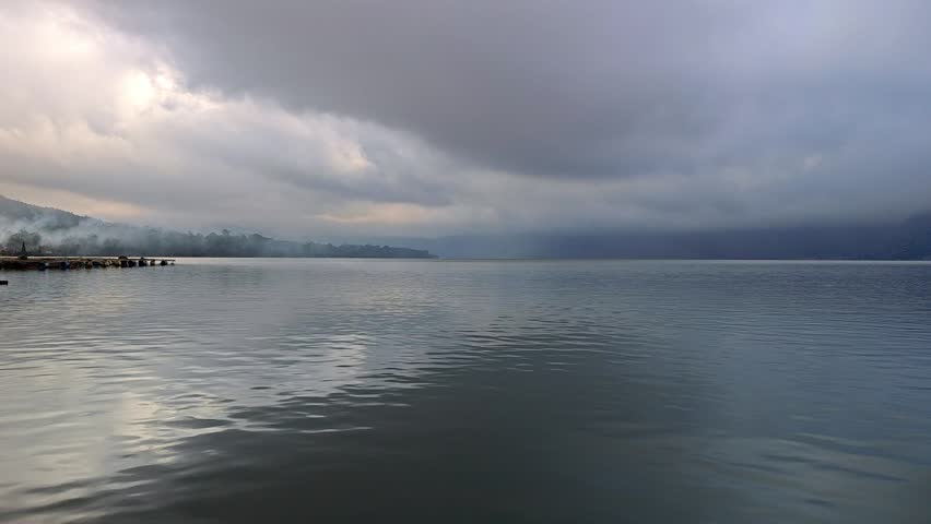 Calm Lake Waters under Moody Dark Cloudy Sky with Misty Distant Shore