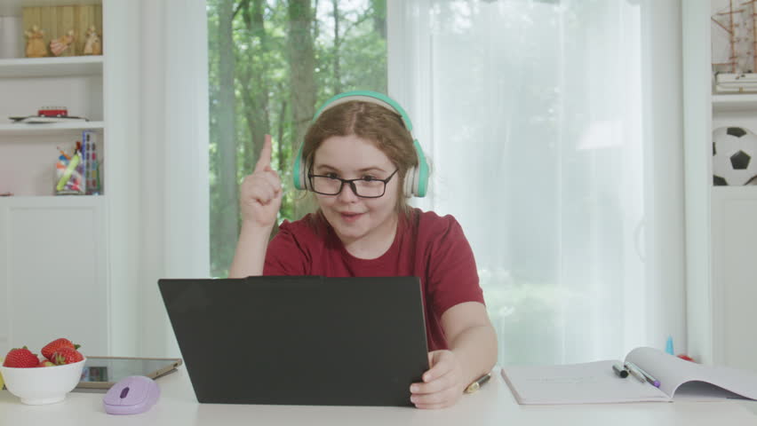 Excited child studying online with headphones and laptop during home school lesson. School child with idea learning. School child raising finger with idea. Education, creativity, solving concept.