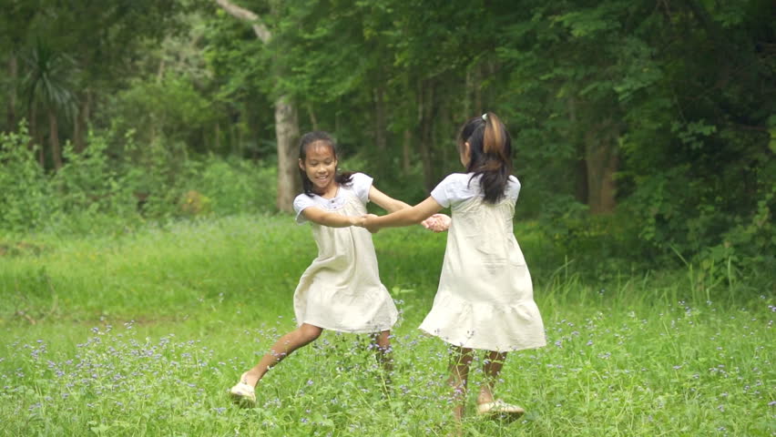 Two happy Asian girls holding hands and spinning around in a wild flower field