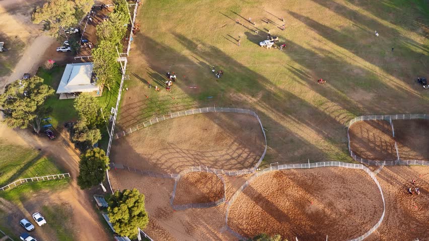 High-angle drone shot of equestrians practicing in a fenced arena in Coonabarabran, Australia.