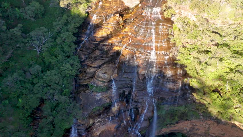 High-angle drone shot of Wentworth Falls flowing over rocky cliffs in Blue Mountains National Park.