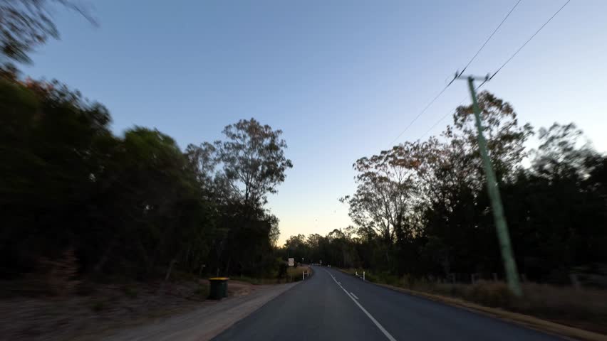 Motion blur captures a red car speeding along a forested road in Pillar Valley, Australia.