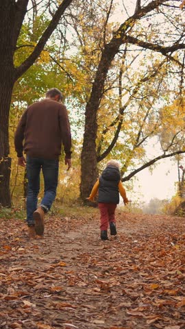Father and child enjoying an autumn walk on a leaf-covered forest path, playing together and sharing joyful family moments in the warm golden seasonal light